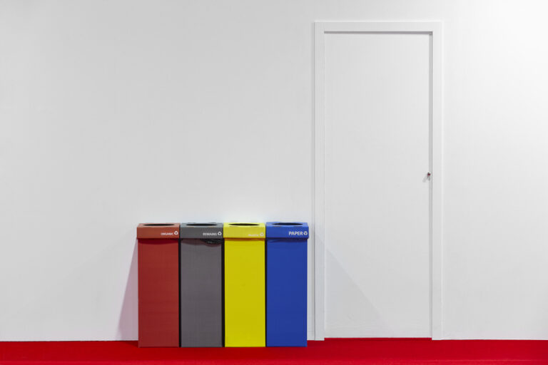 Quatre poubelles de différentes couleurs placées à côté d'une porte