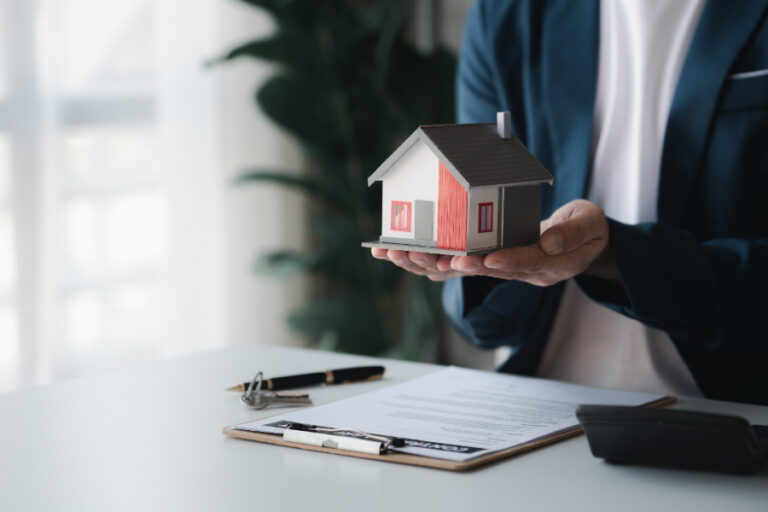 Une personne tenant une petite maison avec des documents d'assurance habitation valable pour quelque temps sur la table