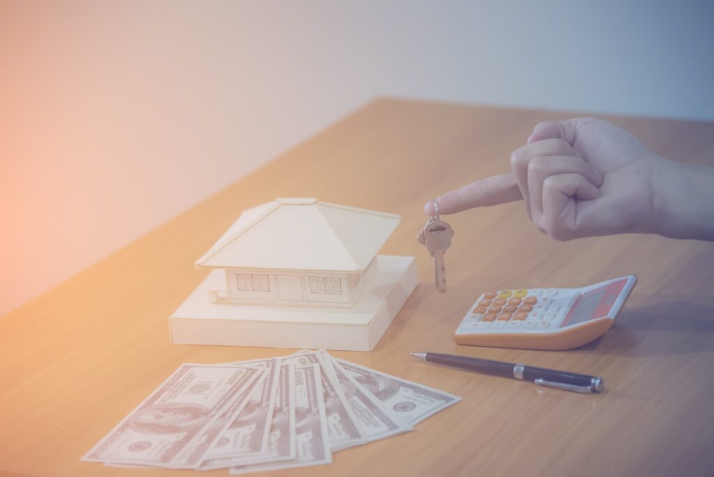 Un agent immobilier qui tient une clé devant une modèle de maison avec des argents et une calculatrice