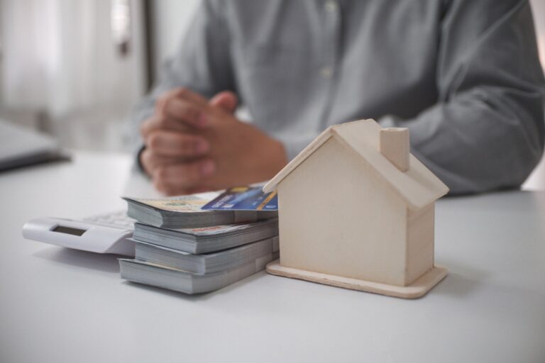Une personne assise avec un modèle de maison et des monnaies sur la table
