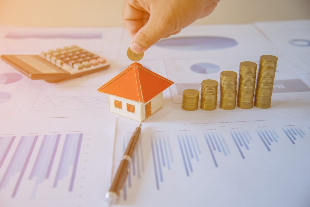 Pile de pièces, calculatrice, stylo et une maquette de maison sur la table