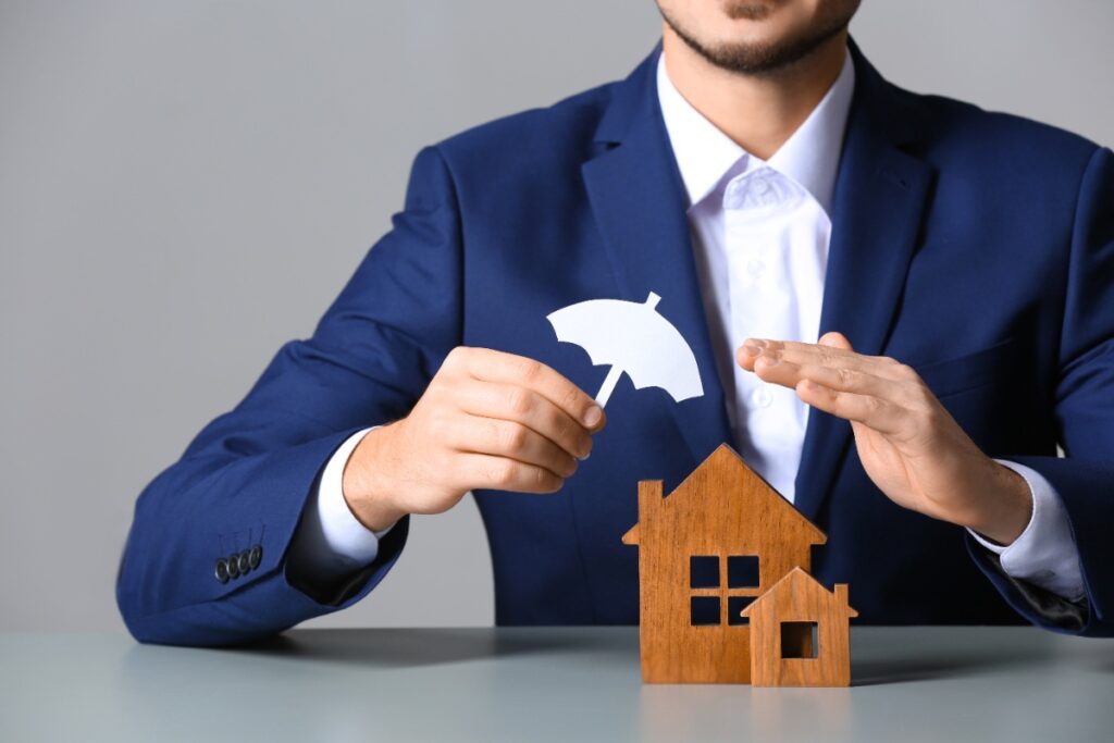 Un agent immobilier avec une petite maison sur la table, présentant une assurance habitation