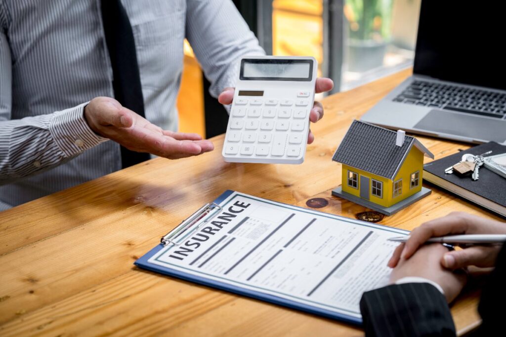 Un agent immobilier tenant une calculatrice et discute avec une personne concernant l'assurance habitation