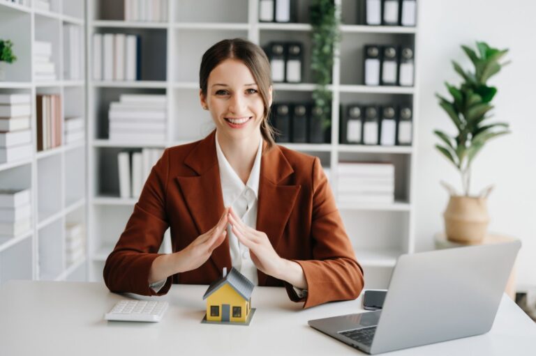 Une femme assise dans son bureau avec un ordinateur et une maquette de maison sur la table