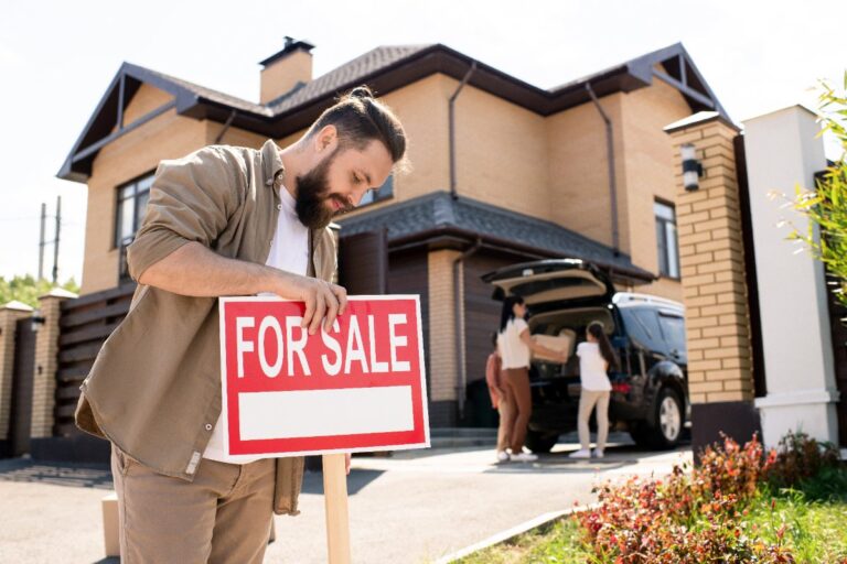 Un homme plaçant un panneau à vendre devant une maison