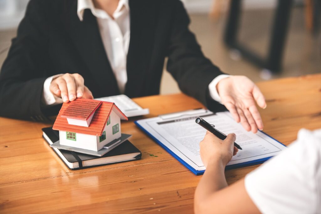 Un agent immobilier et une personne qui signe un contrat immobilier sur la table