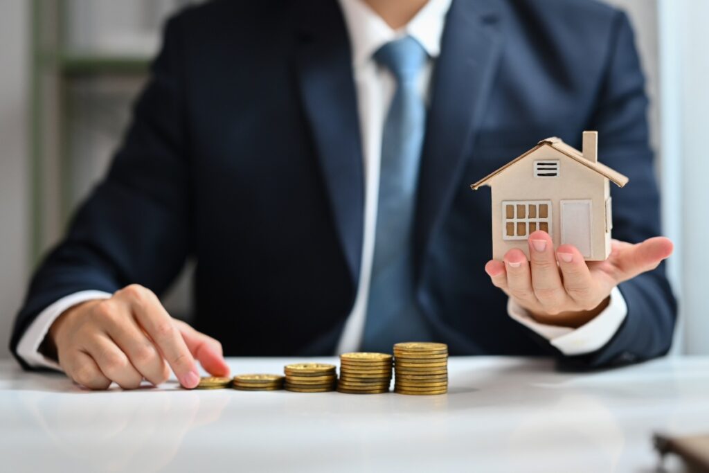 Un agent immobilier tenant une maquette de maison avec des argents sur la table
